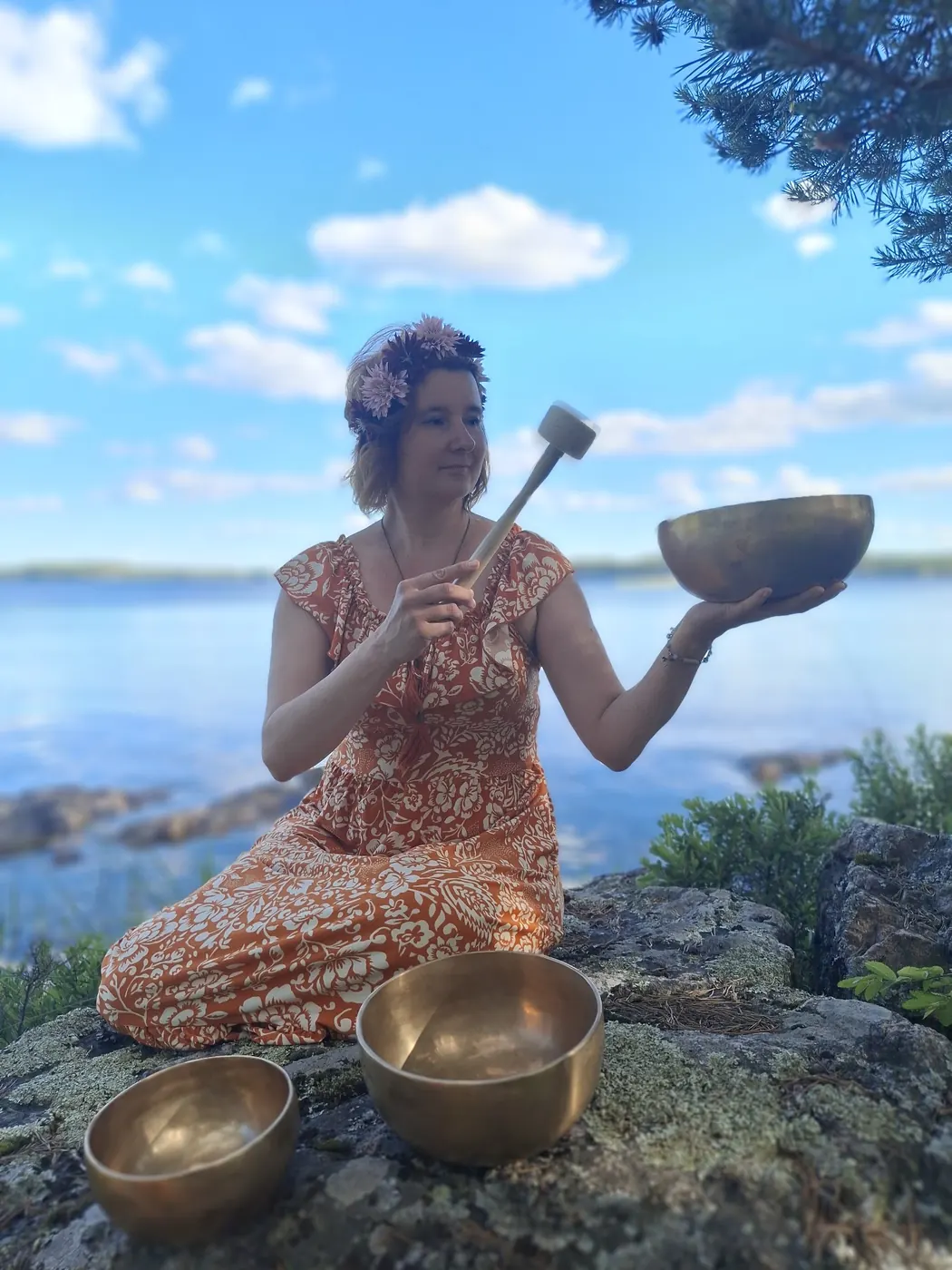Äänimaljojen soittaja kallioilla järven rannalla, malja kädessä