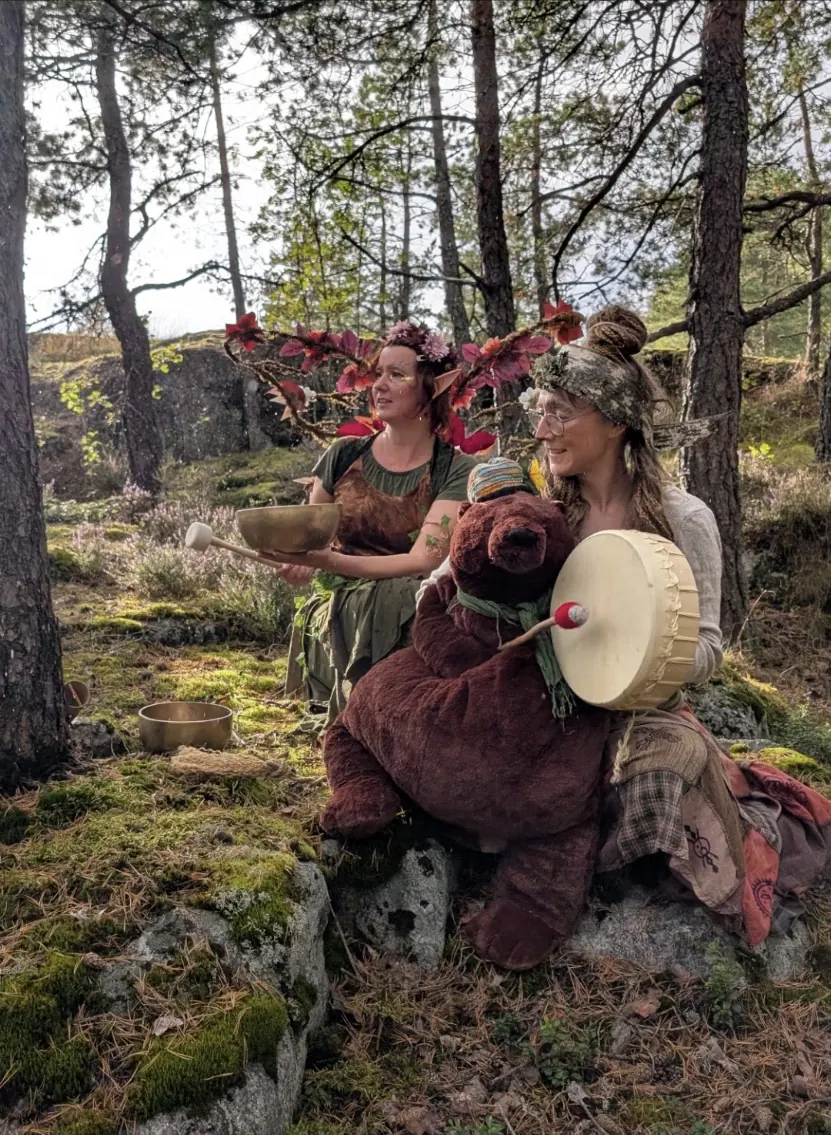 Keiju Aarnitar soittaa äänimaljaa metsässä, vieressä rumpua soittava esiintyjä ja iso nallekarhu
