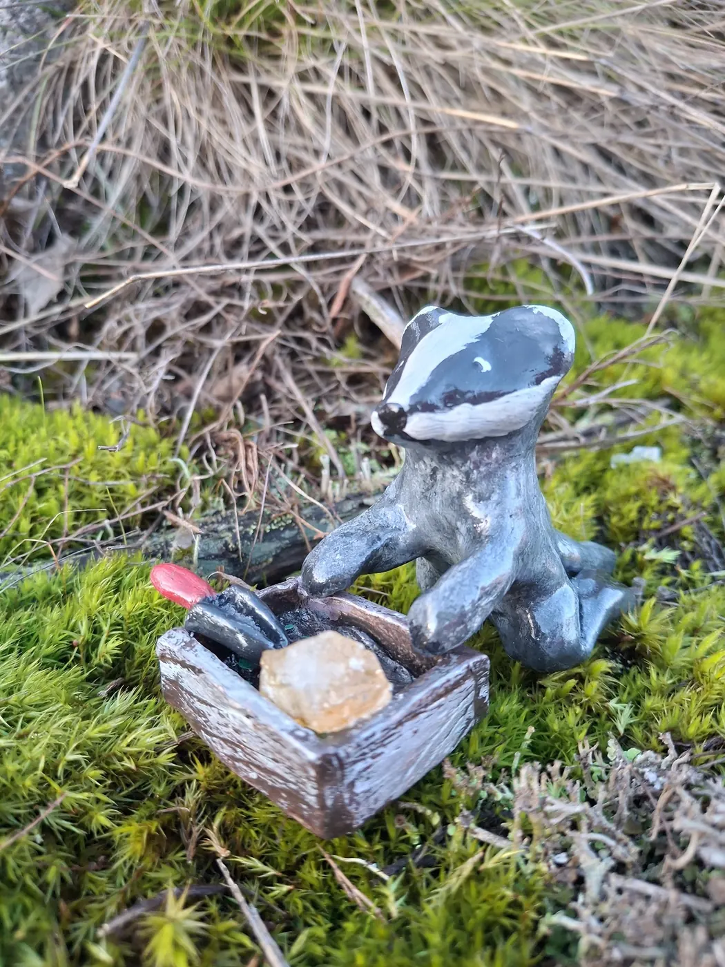 Mäyrä istuu puisen arkun luona, arkussa kristalleja